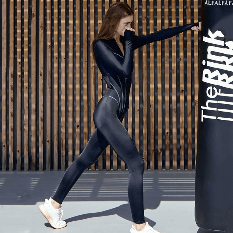 Woman in sexy long sleeve sports jumpsuit with front zipper SF1061, exercising by punching bag in sleek, durable polyester fabric.